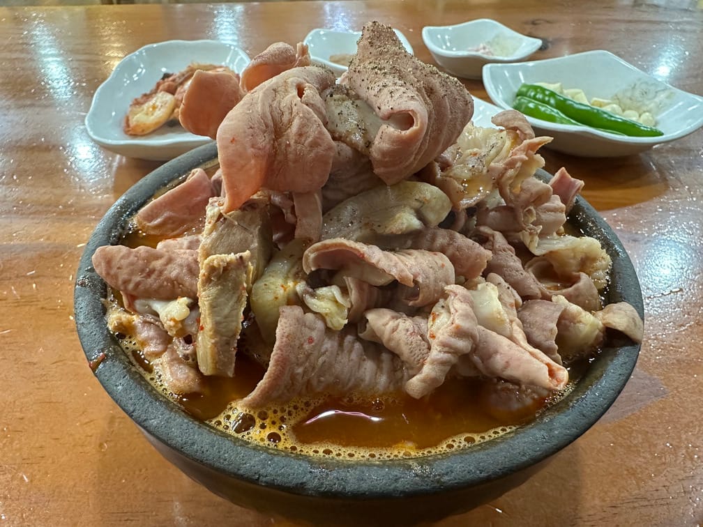 뚝배기 안에 붉은 국물이 가득 차 있고, 산더미처럼 쌓인 돼지부속 고기가 그 위에 있고 후추가 뿌려져 있다.