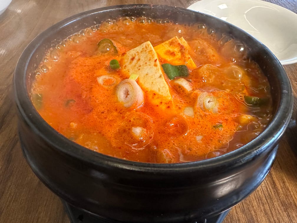 뚝배기 안에 끓고 있는 붉은 국물 위로 썬 파, 두부 등이 보인다.
