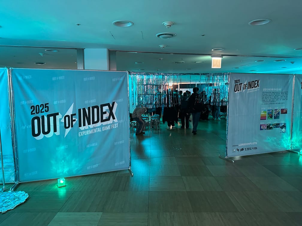행사 Out of Index 2025 행사장의 진입통로 사진. 현수막으로 쳐진 벽과 은박지로 된 발 너머에 사람들이 다니는 행사장 사진.