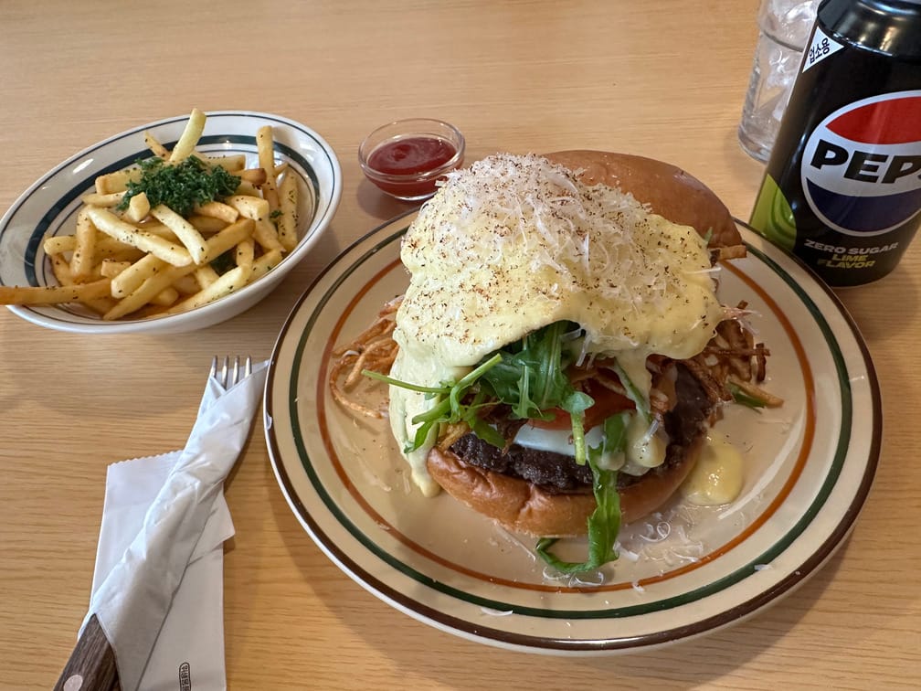 흰 소스가 넘치게 올라간 버거, 감자튀김, 케첩, 제로콜라가 차려진 테이블의 사진.