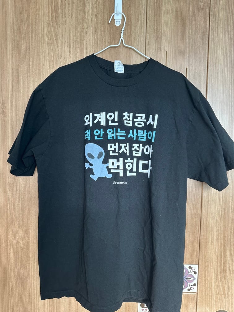 "외계인 침공시 책 안 읽는 사람이 먼저 잡아먹힌다"라는 문장과 하늘색 외계인 모양의 도안이 가슴 부분에 있는 검은 티셔츠.