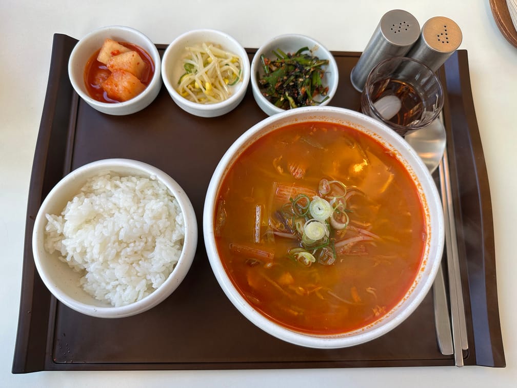 쟁반 위에 차려진 붉은 국물 요리,흰밥, 깍두기, 콩나물, 부추김치, 매실차, 소금과 후추통.